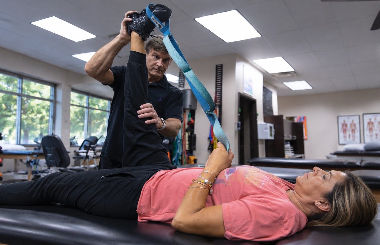 Advanced Health Solutions therapist guiding a woman through an assisted hamstring stretch with a strap in the rehab gym