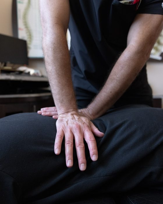 Advanced Health Solutions chiropractor with crossed hands pressing on the back of a face-down patient, a spine chart in the background