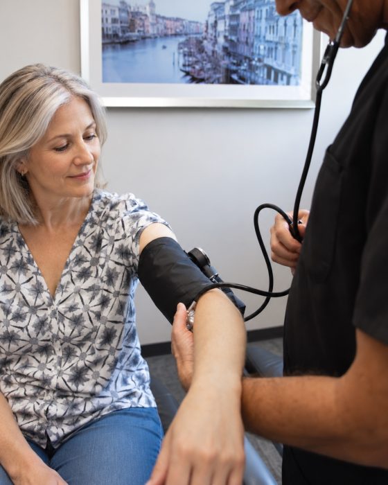 Advanced Health Solutions clinician measuring blood pressure for a smiling woman seated in an exam room