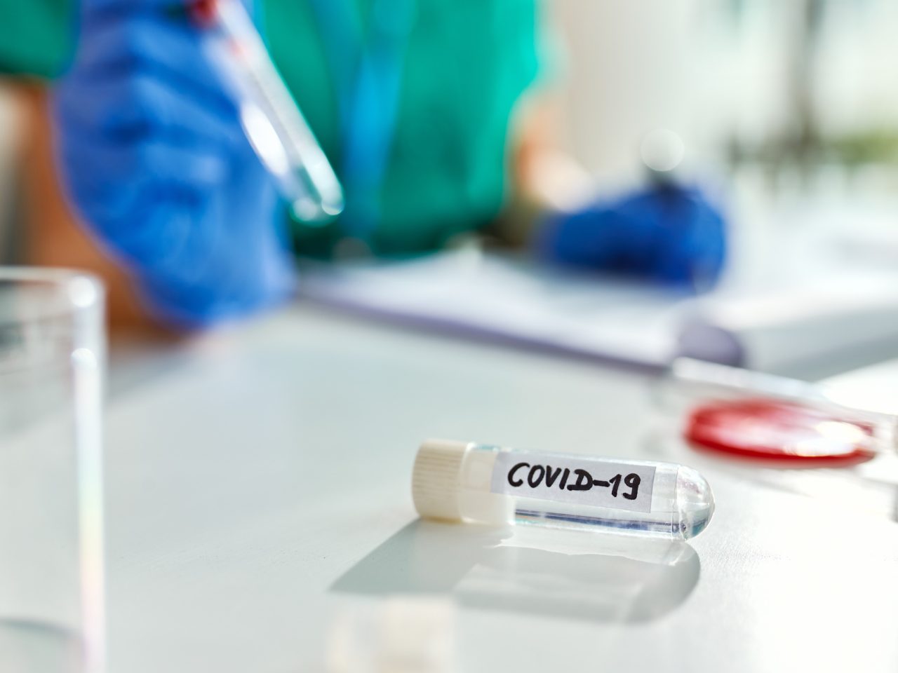 Advanced Health Solutions: test tube with a coronavirus sample, lab worker in the background