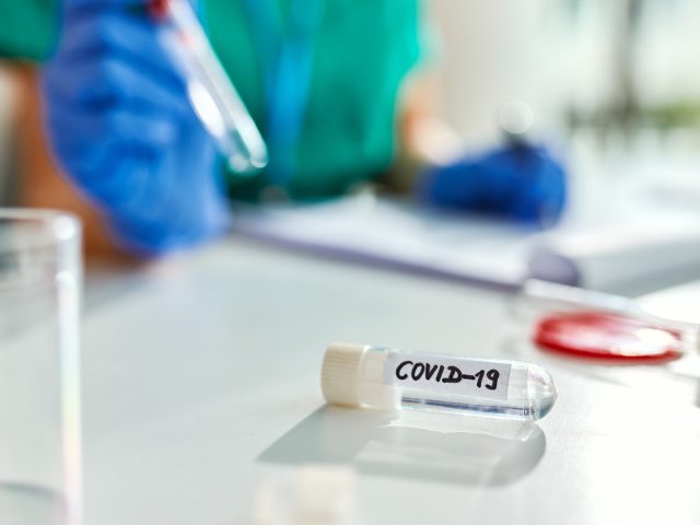 Advanced Health Solutions: test tube with a coronavirus sample, lab worker in the background