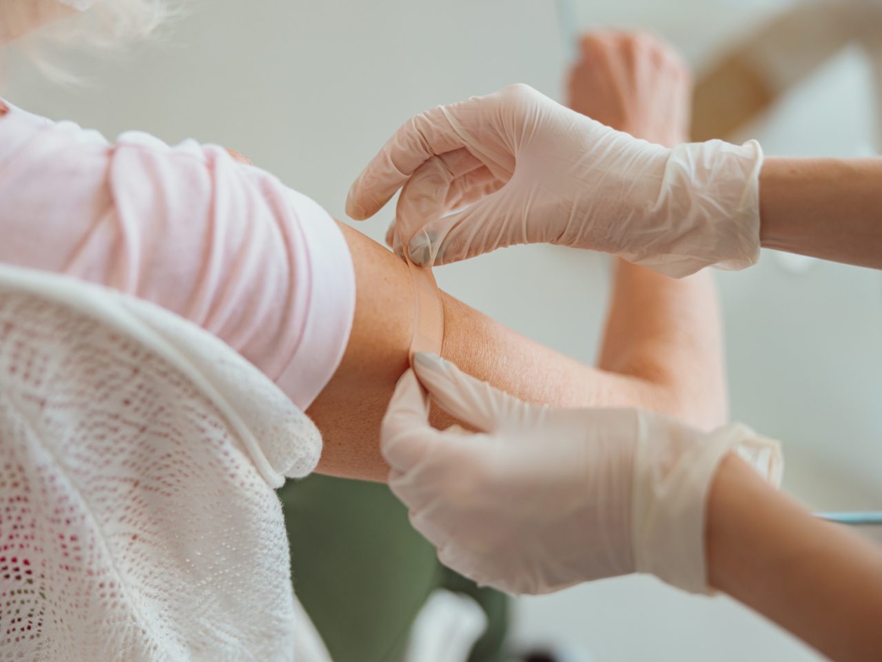 Advanced Health Solutions: gloved healthcare worker applying a bandage to an older patient's shoulder after an injection